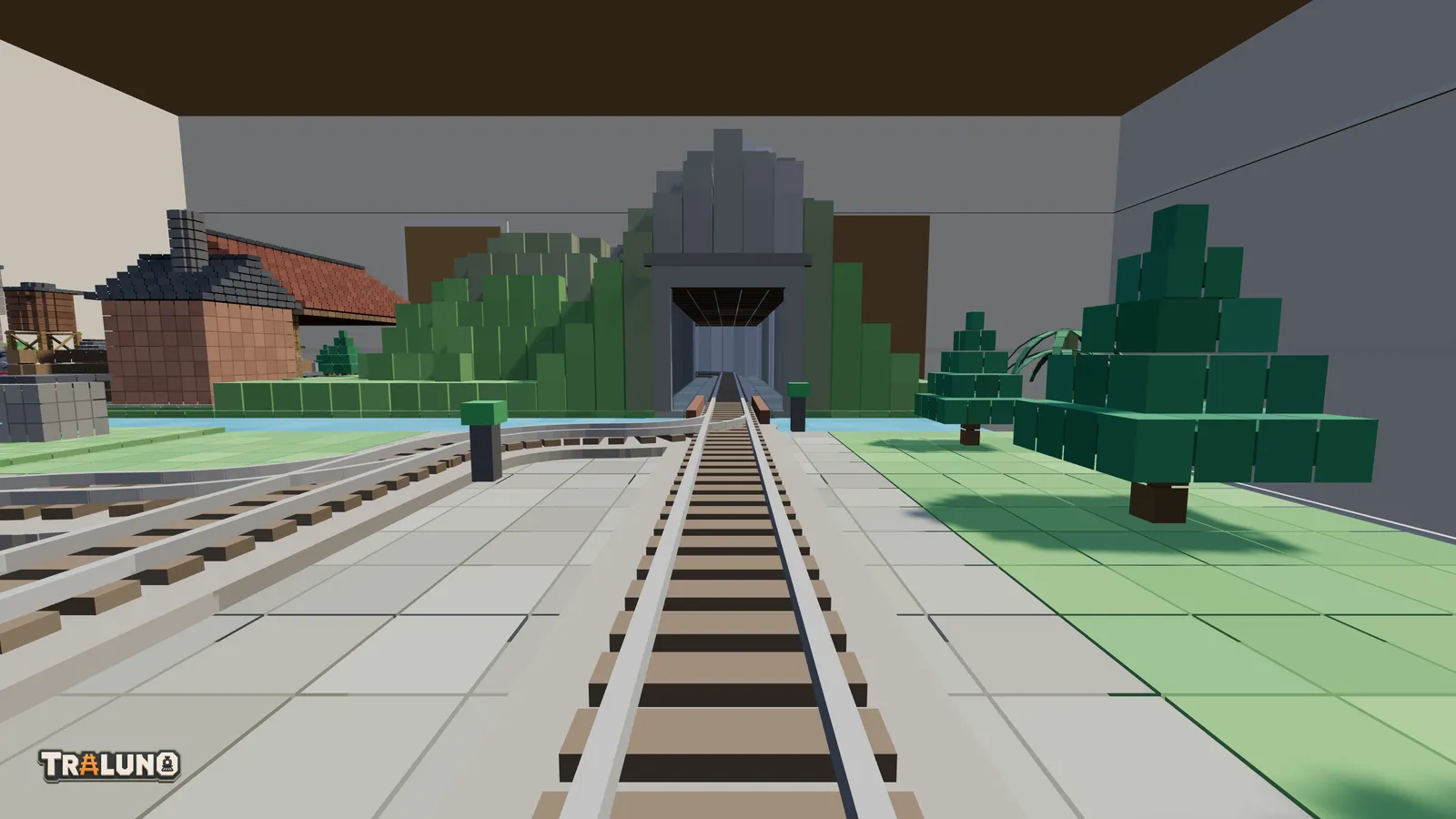 The view at rail height from the front of a train: the track runs ahead past a yard track joining from the left, over a short bridge and into a stone tunnel portal in a blocky green mountain, with the wall of the room behind.