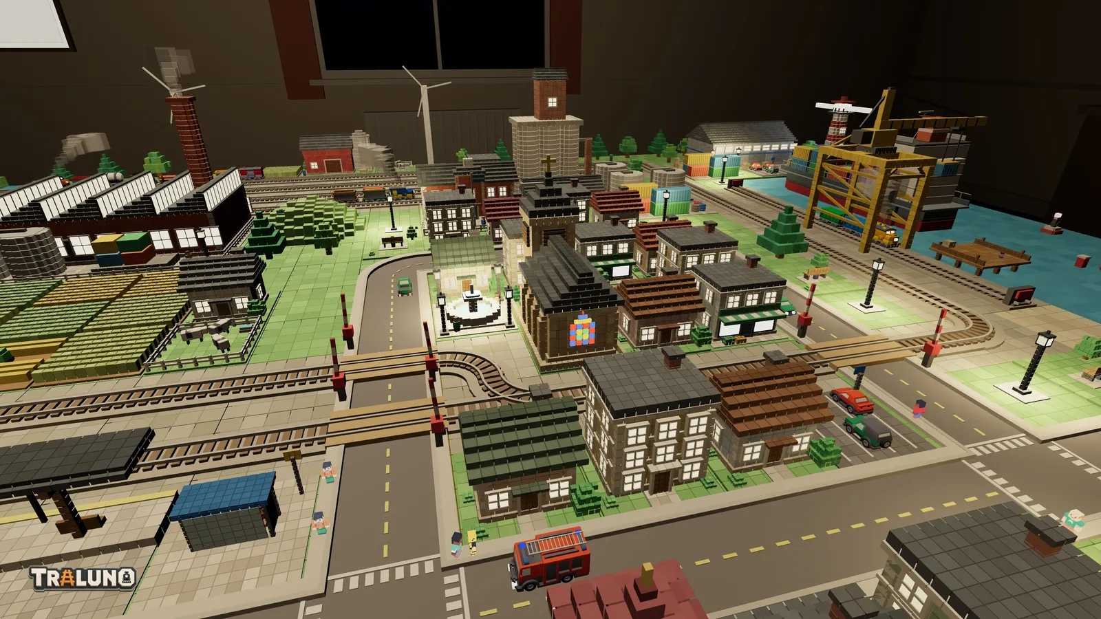 The town on the demo layout at night, with lit windows in the houses and the church, street lamps glowing on the pavements, the fountain square lit, and the harbour crane dark behind.