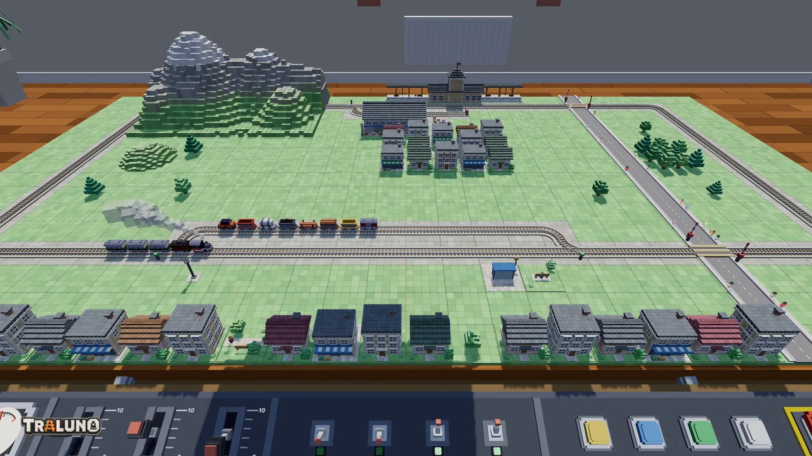 The plan seen from the Stand view at the front edge of the table: a row of houses and the control desk in the foreground, the passing loop with two trains in the middle, and the mountain, the town block and the station small at the back.
