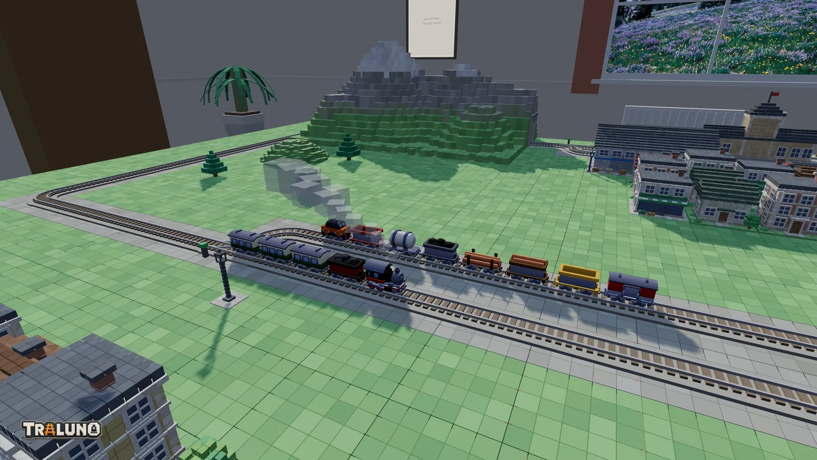 A plan tried out on a Traluno table: a steam train runs along the front straight past a goods train waiting in a passing loop, with a blocky mountain, a town block and a station roughed in behind.