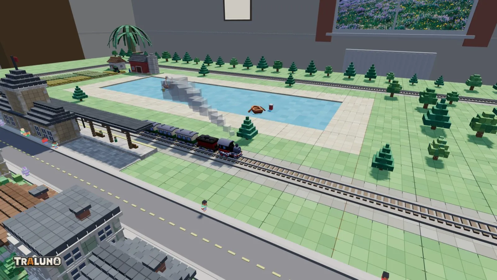 A view of a small layout as the screenshot tool returns it: a steam train with three coaches leaving a station beside a lake with two boats, a street and houses in front, rows of trees behind, and the Traluno wordmark in the corner.