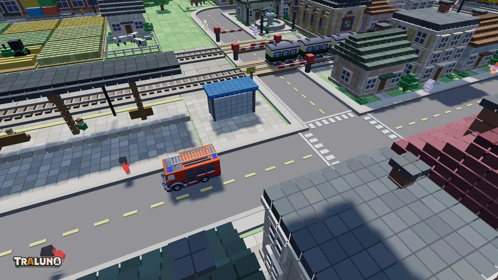 A close view of the demo town's front street: a red fire engine on the road, a bus shelter and the station platform beside it, striped crossings at a junction, and small figures walking on the footways and near the level crossing.