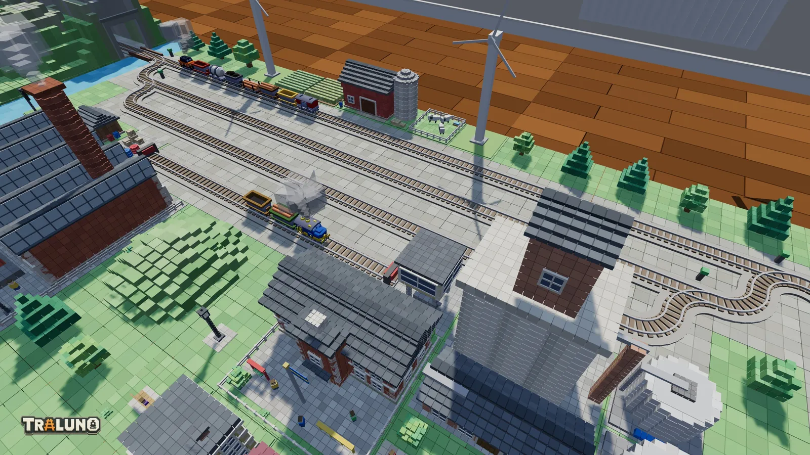 The goods yard on the demo layout from above: parallel yard tracks with a ladder of switches at each end, a long goods train on the main line behind them, a small blue locomotive with two wagons on a yard track, and a factory and a grain elevator in front.