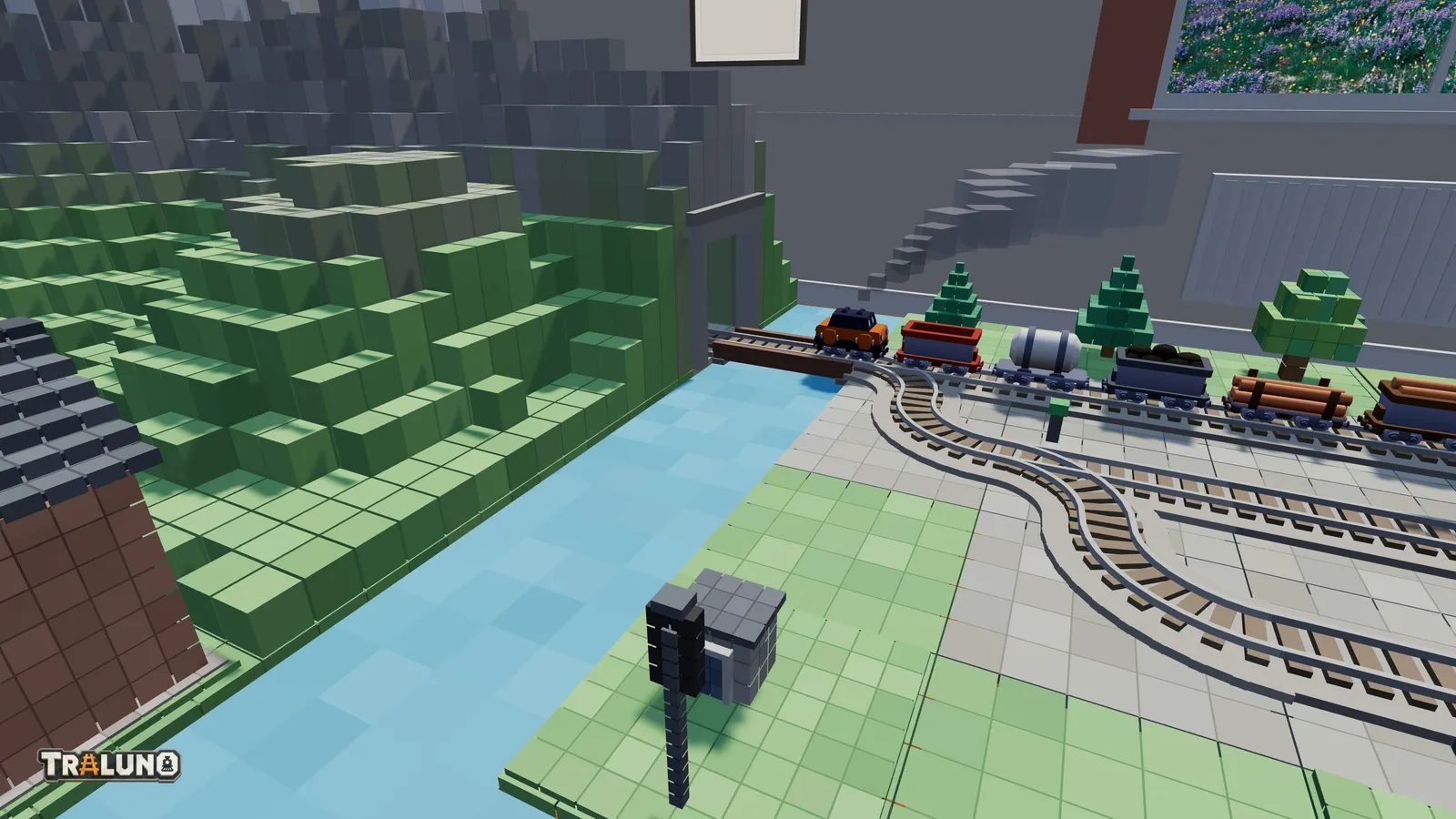 A goods train on a short bridge over a strip of water at the back of the table, its locomotive at the stone tunnel portal of a blocky green and grey mountain, with yard tracks curving away in front.