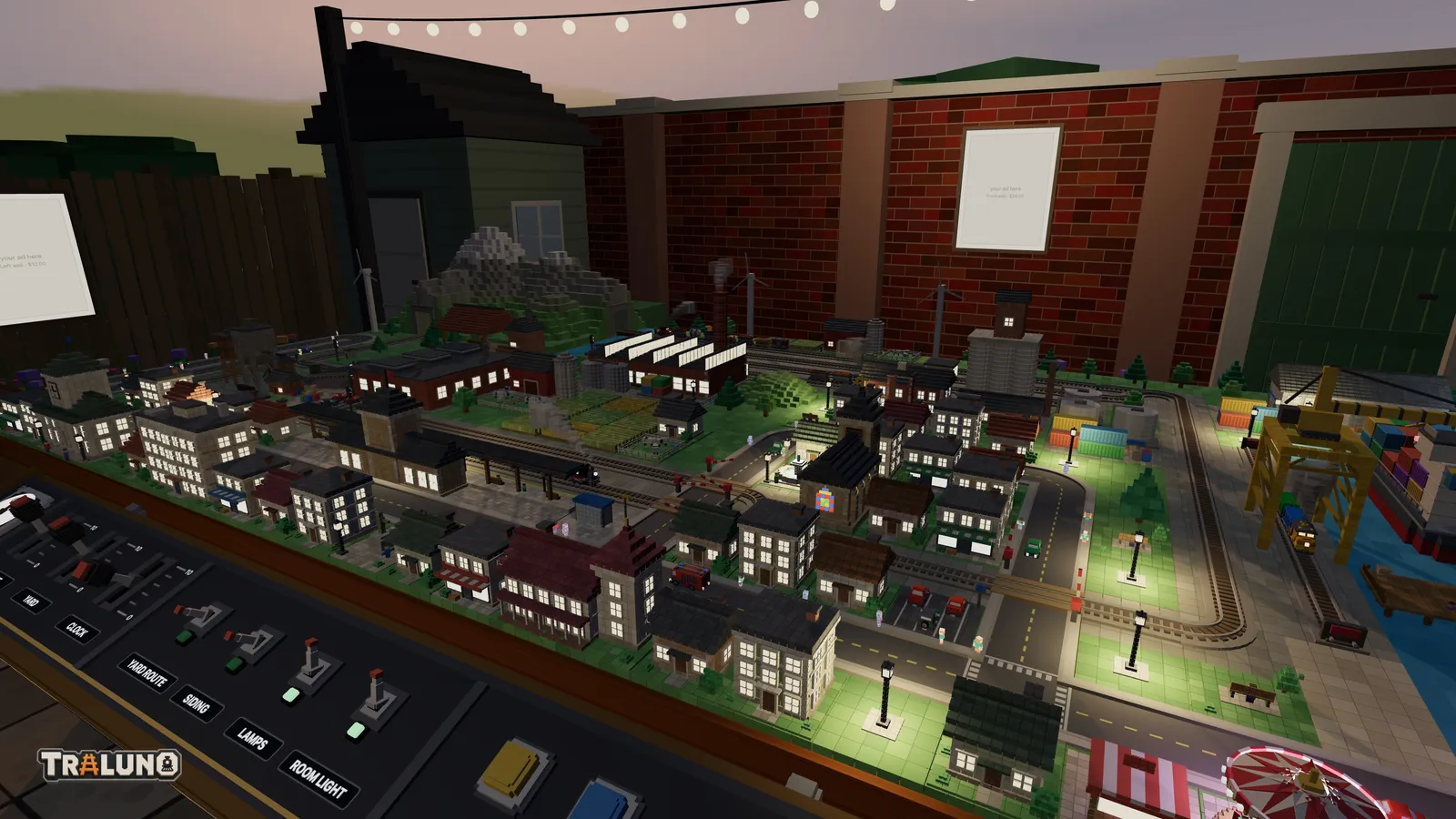 The demo layout in the garden at dusk, seen over the control desk: a pink and violet sky above the brick wall and the shed, festoon bulbs glowing along the top, and the town below with its windows lit and its street lamps throwing pools of light.