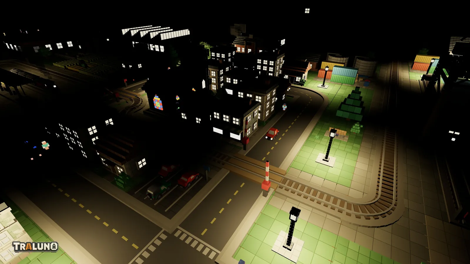 The town at night with the room light off: house windows glow as bright panes while the walls around them stay black, and street lamps cast pools of light on the grass and paving beside a level crossing.