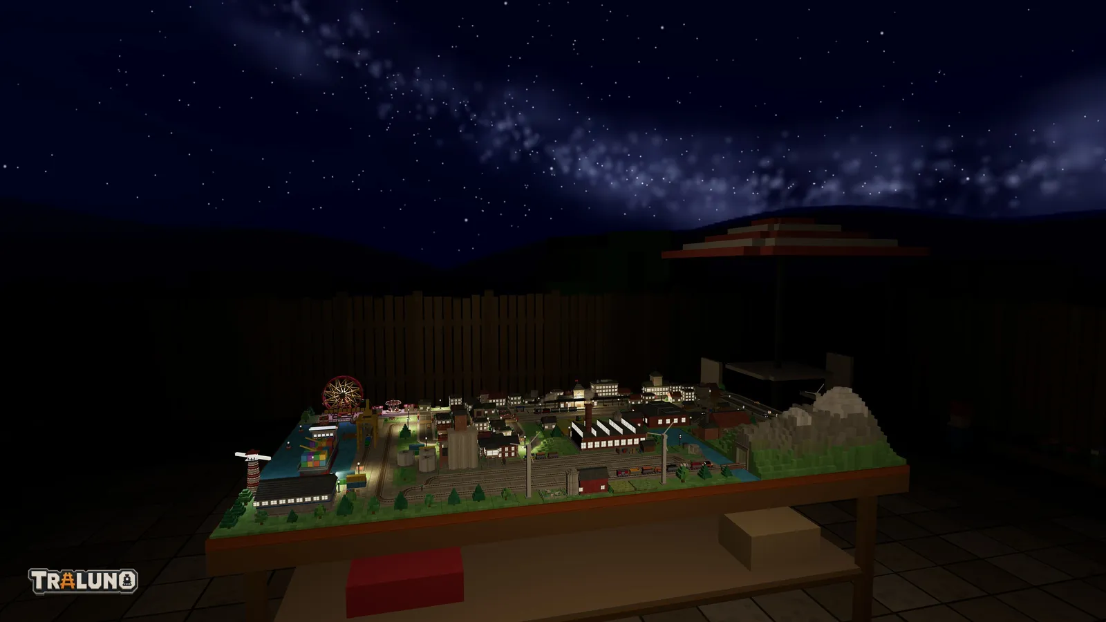 The garden at night seen from behind the table: the band of the Milky Way crossing a sky of small round stars, the dark line of the painted hills above the fence, a parasol, and the layout lit below.